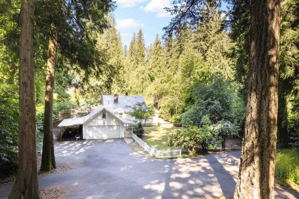 This photo captures the home nestled among mature trees, with the driveway leading up to it. The scene spotlights the property’s peaceful location and harmonious blend with its natural surroundings, reinforcing a sense of seclusion and environmental mindfulness.