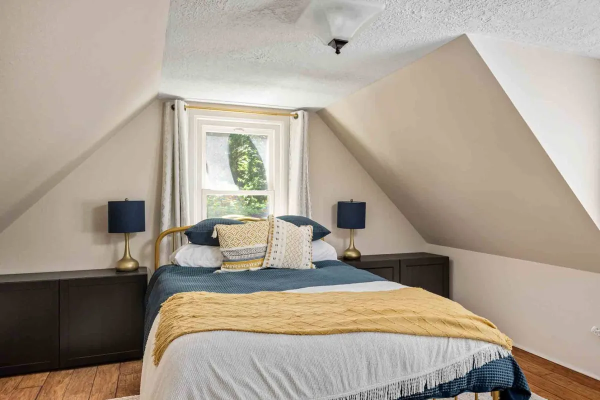 A cozy bedroom featuring blue and yellow bedding on a comfortable bed, dual bedside lamps, and gentle sunlight pouring in through the window, evoking a sense of warmth and relaxation.