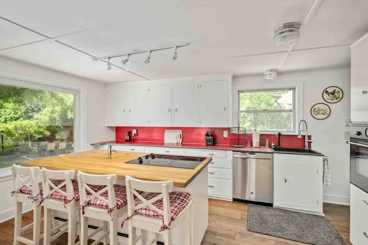 A warm and welcoming kitchen scene with a wooden island, a bold red accent wall, and crisp white cabinetry. The setting exudes a sense of homely comfort, perfect for cooking, entertaining, and gathering around for family moments.