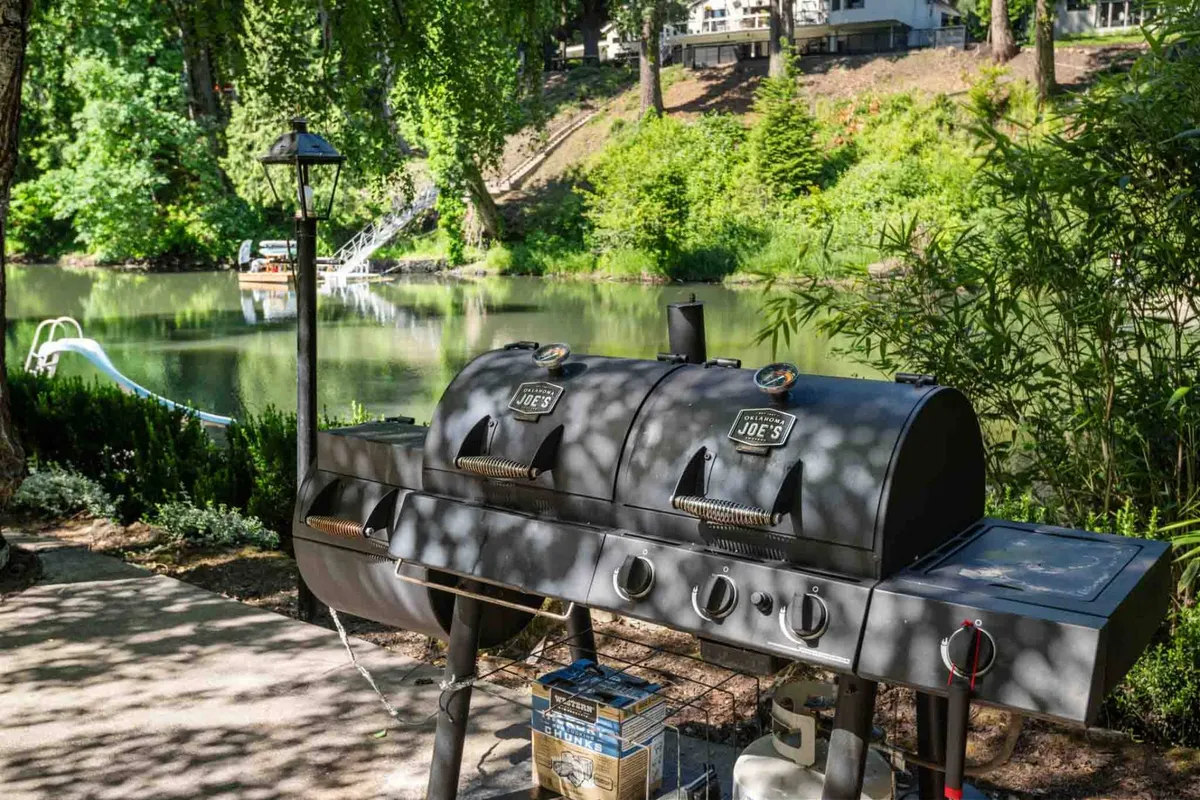 A scenic grilling area with a BBQ grill nestled among lush greenery and overlooking a tranquil water body. The setting invites outdoor cooking and relaxation, offering a seamless blend of natural beauty and functional space.