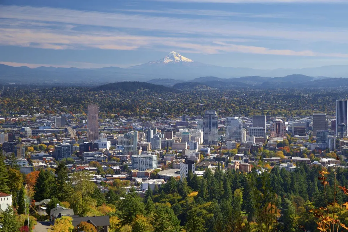 A panoramic view of the city skyline set against the majestic backdrop of Mount Hood, surrounded by vibrant autumn foliage. The scene captures people enjoying nearby hiking trails and scenic city parks, emphasizing the accessibility of both natural beauty and urban exploration.