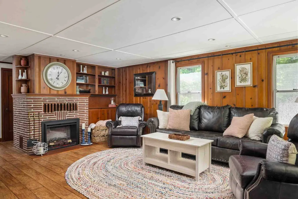 A cozy living room featuring a classic fireplace, a soft area rug, a comfortable sofa, and a well-stocked bookshelf. Warm wooden tones and vintage accents evoke the home's 1930s charm, while the inviting layout encourages relaxation, reading, and social connection.