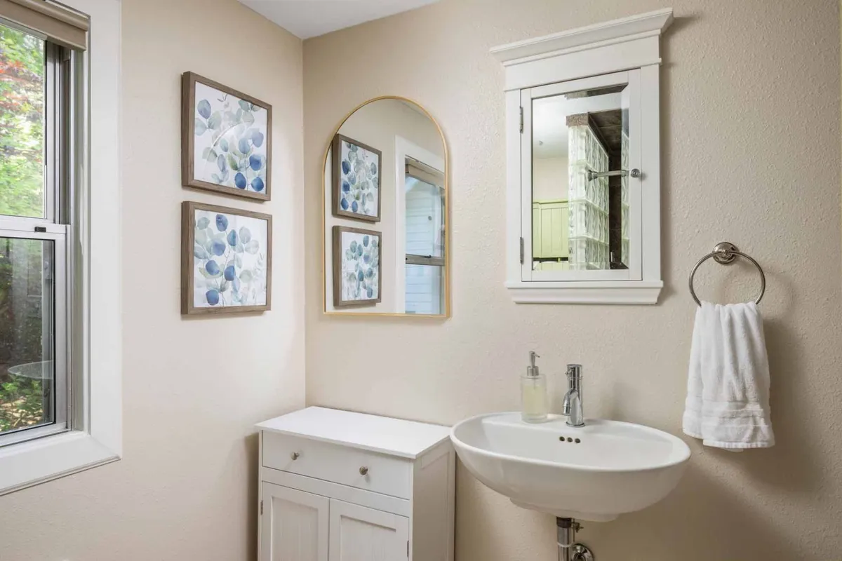 A stylish bathroom with a modern sink, round mirror, and framed artwork above. The room is illuminated with gentle light, evoking cleanliness and a touch of elegance.