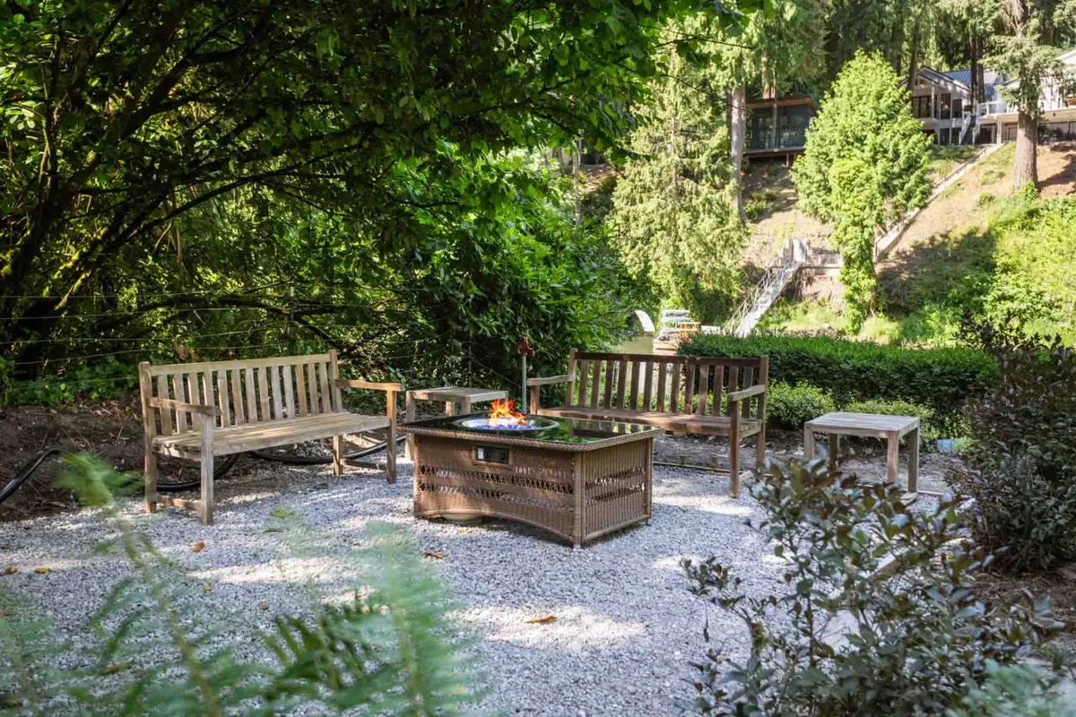 This inviting exterior scene features a glowing fire pit area with wooden benches set in natural surroundings, creating a cozy outdoor gathering space. The setting is perfect for star-gazing, socializing, or unwinding by the fire after a day on the river.