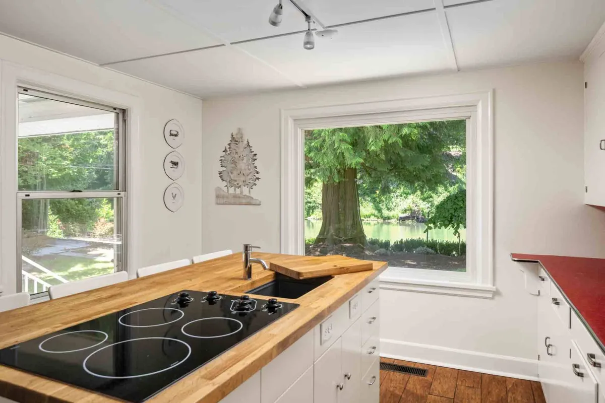 A welcoming kitchen with a spacious island, modern stove, decorative plates on the walls, and a large window showcasing tree-filled views. The combination of classic details and updated appliances demonstrates the blend of vintage character and modern functionality.