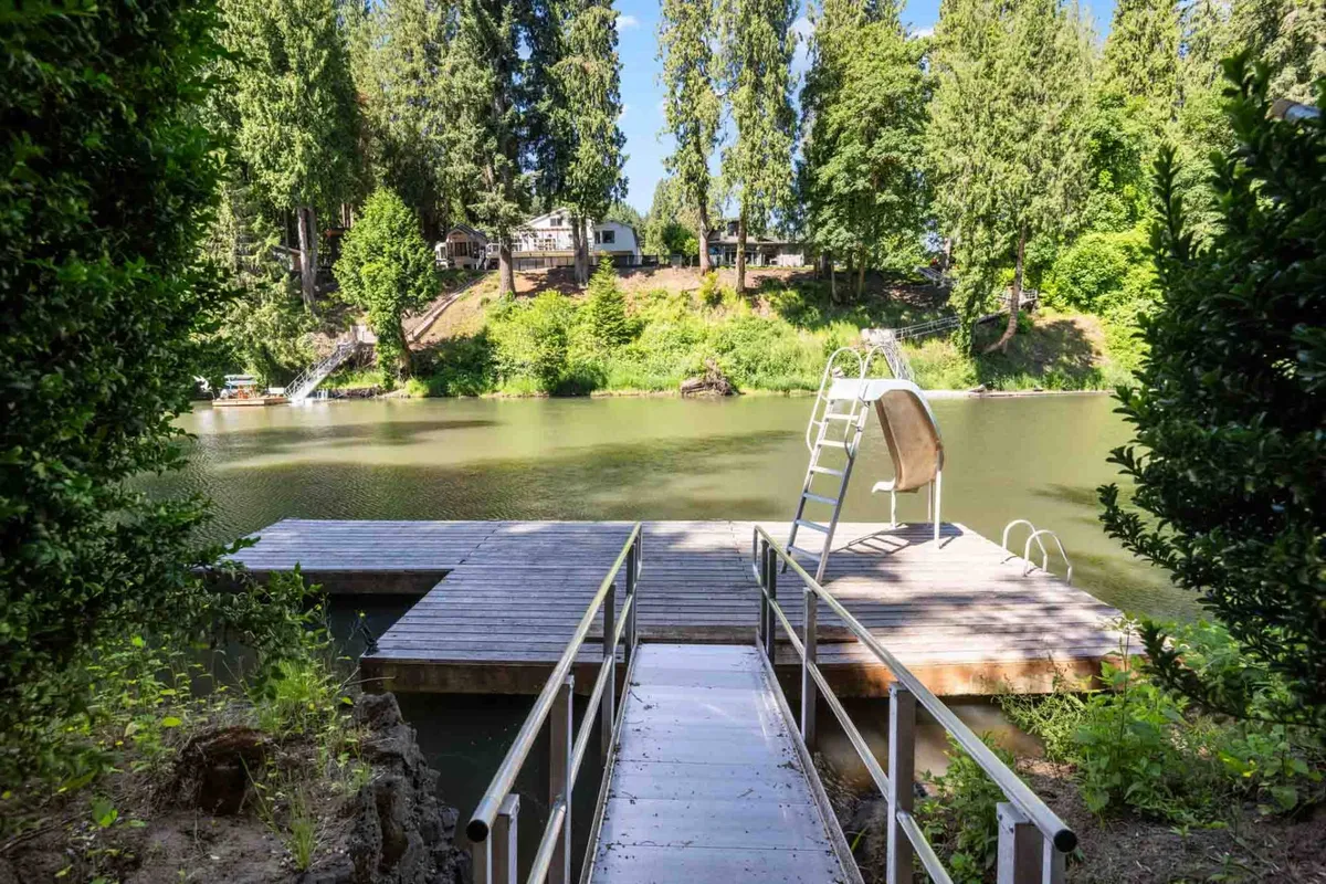 This close-up of a wooden dock with a swimming ladder, surrounded by lush greenery and calm water, highlights an intimate riverside spot ideal for quiet reflection, swimming, or launching a kayak. The peaceful ambiance is perfect for relaxation and outdoor wellness activities.